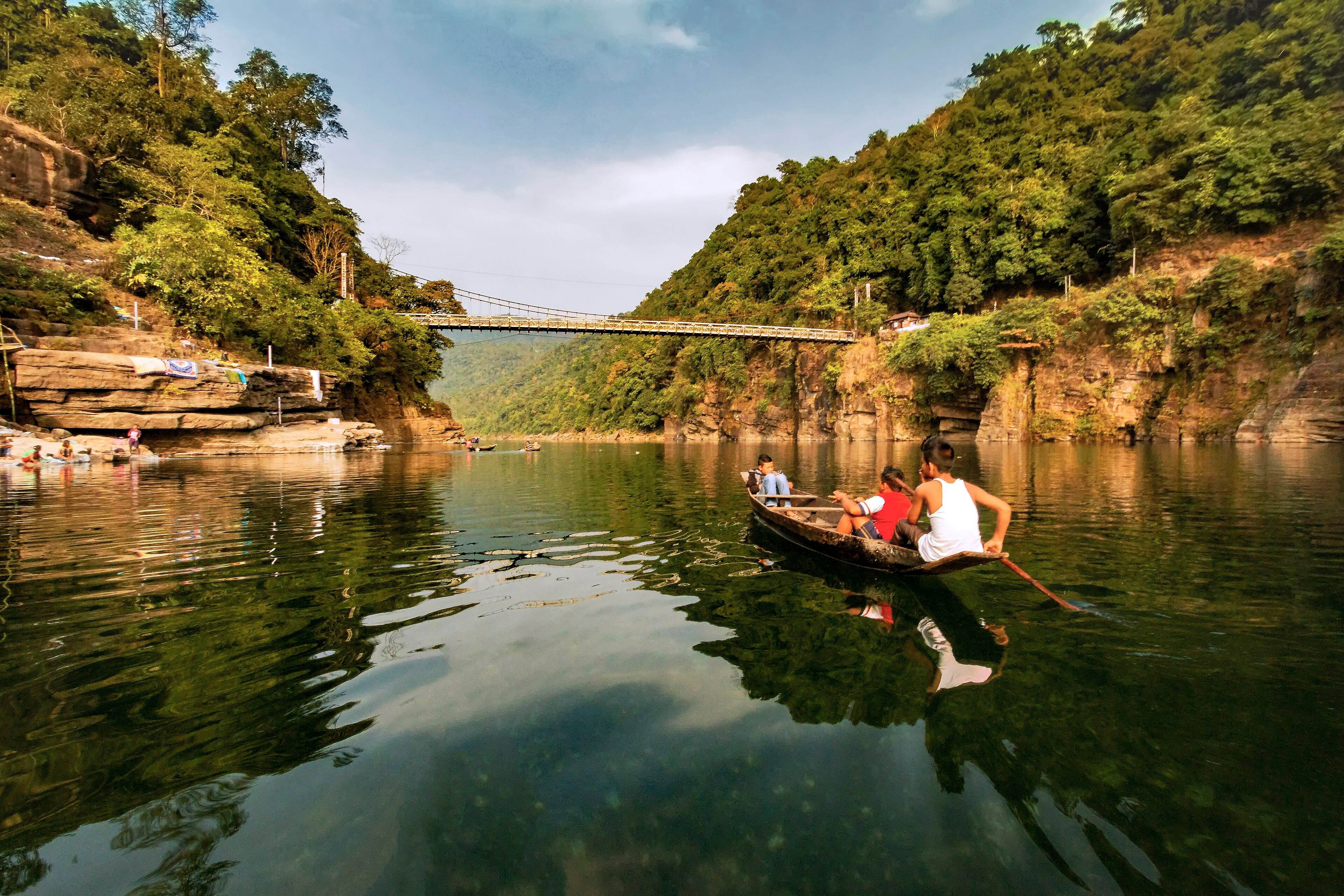 Travellers on a boat ride along the Umngot river below a suspension bridge