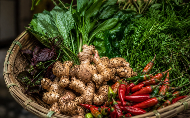"A cinematic close-up of a traditional Khasi conical bamboo basket filled with fresh organic ginger, chilis, and wild forest greens in Shillong."
