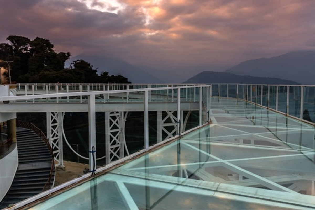 Tourists walking on the transparent Pelling Glass Skywalk with views of the Chenrezig statue in West Sikkim.