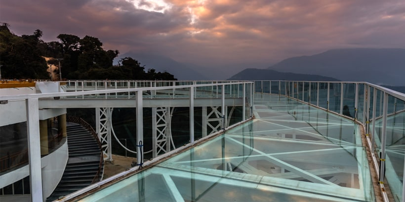 Tourists walking on the transparent Pelling Glass Skywalk with views of the Chenrezig statue in West Sikkim.