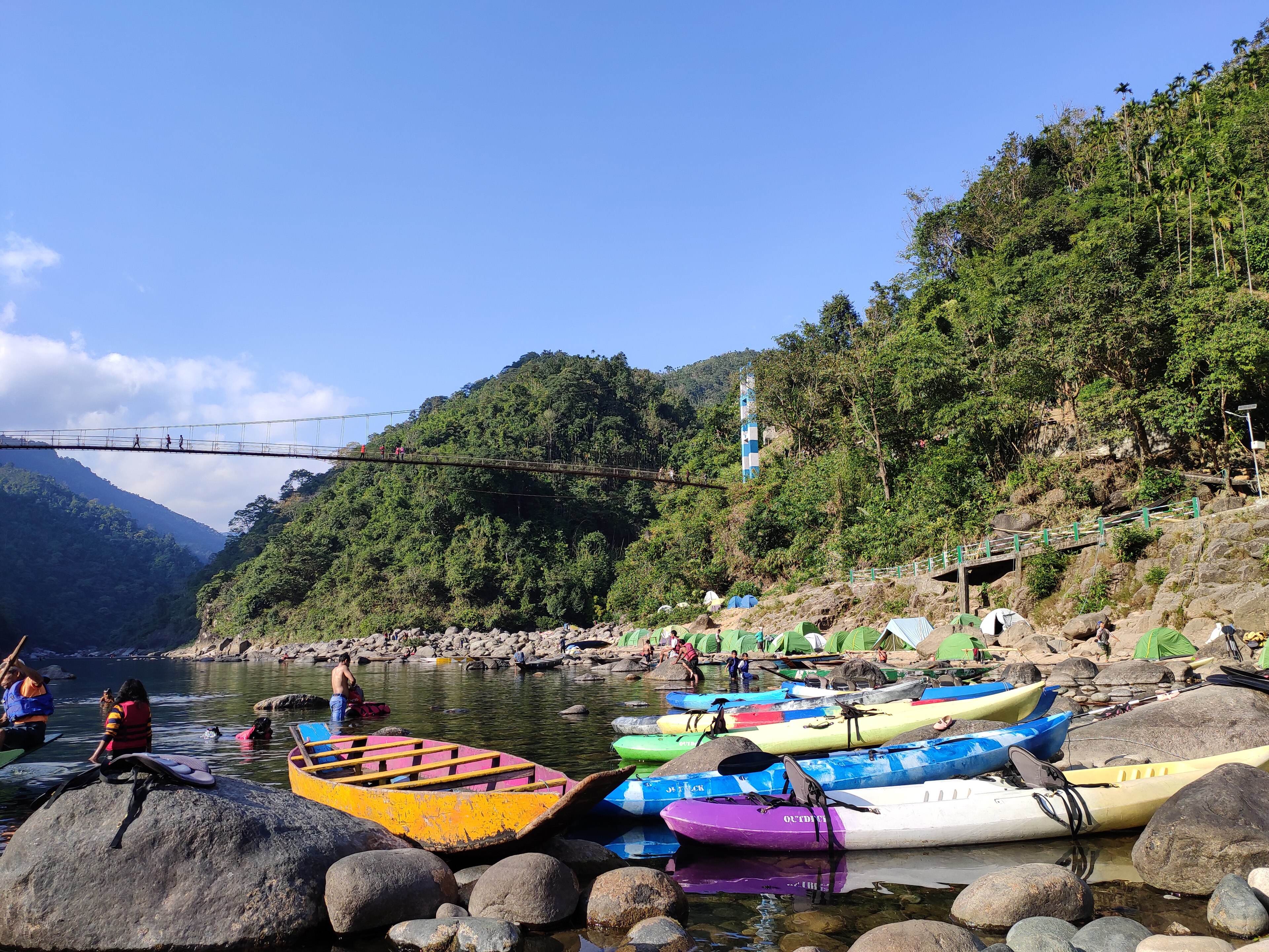 Colourful kayaks pulled up on the Umngot riverbank below a suspension bridge