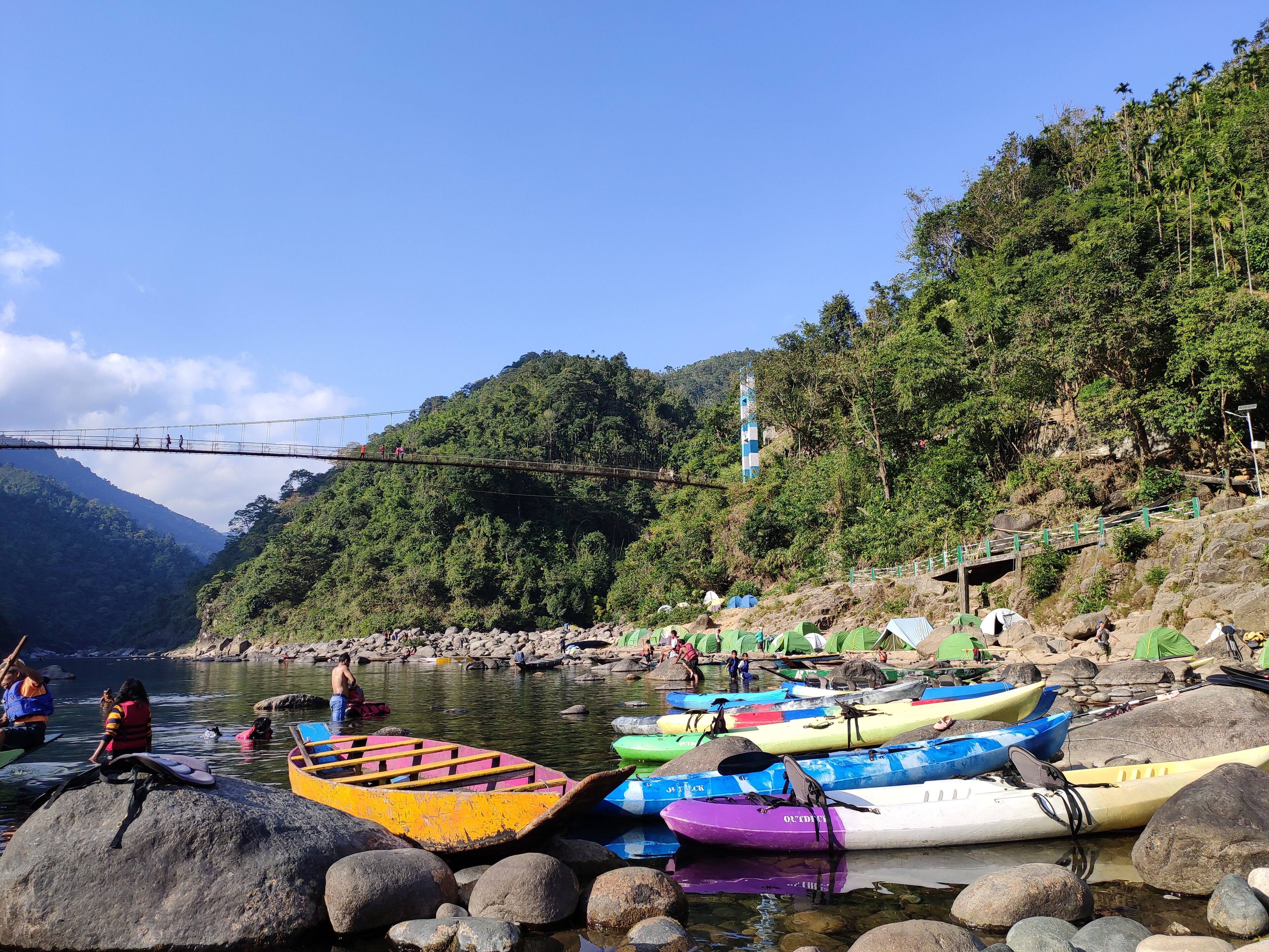 Colourful kayaks pulled up on the Umngot riverbank below a suspension bridge