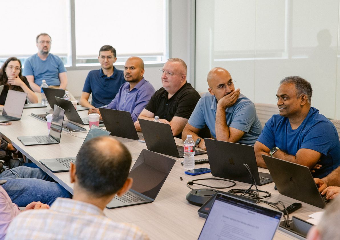 The team around a conference table with laptops, listening to a presentation