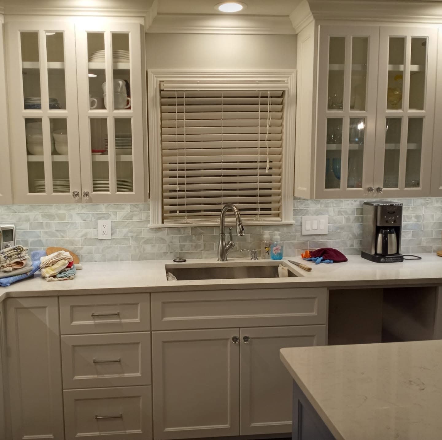 Painted greige kitchen with glass-front upper cabinets and window over the sink
