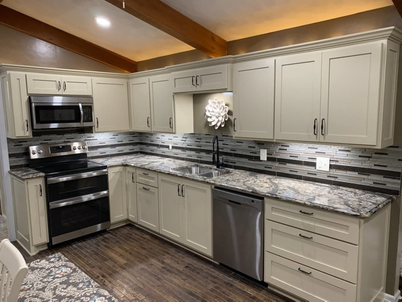 Cream painted kitchen with granite counters, wall oven and exposed beam
