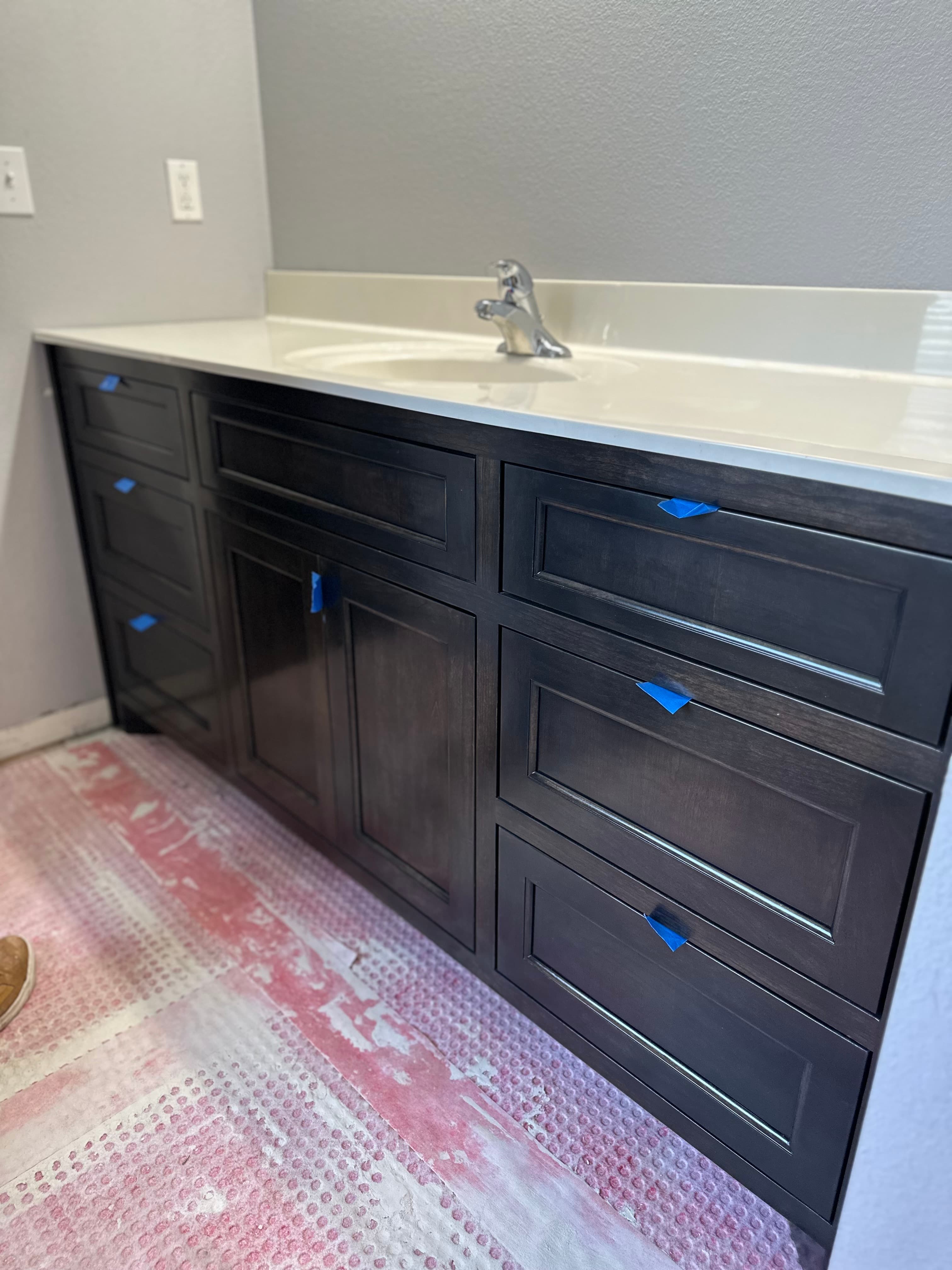 Dark-stained custom bathroom vanity with white countertop, sink, and blue protective tabs during installation