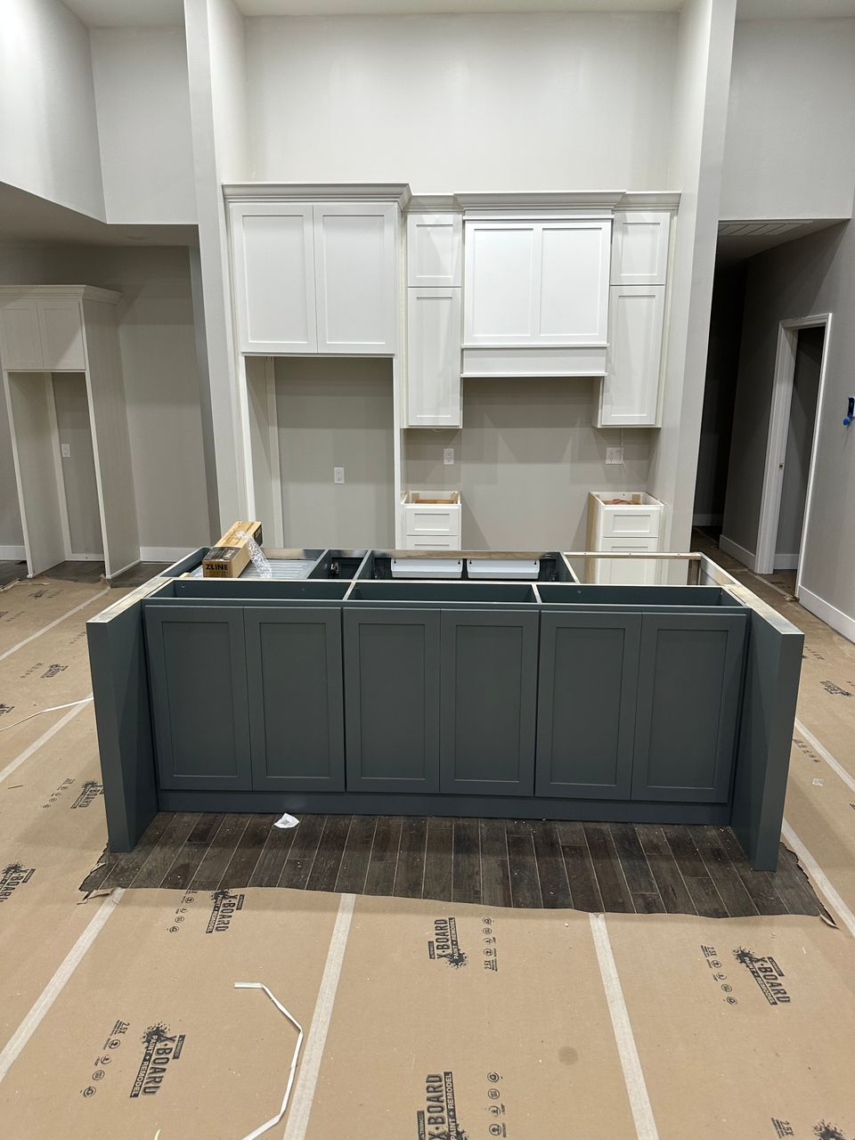 Tall white Shaker kitchen cabinetry and charcoal island arranged symmetrically during installation