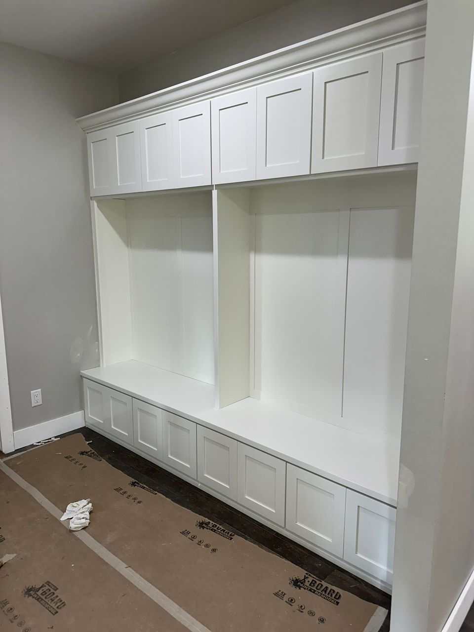White built-in storage wall with upper cabinets, open bays, and bench drawers