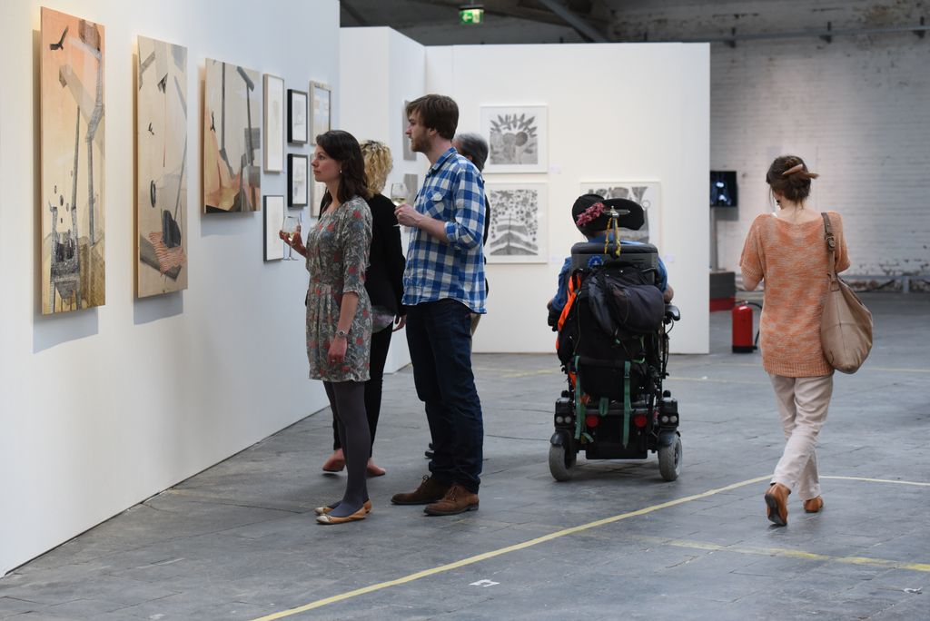 Barrierefreiheit im Kopf 2015: Besucher*innen, darunter ein Rollstuhlfahrer, vor Gemälden in der Ausstellung