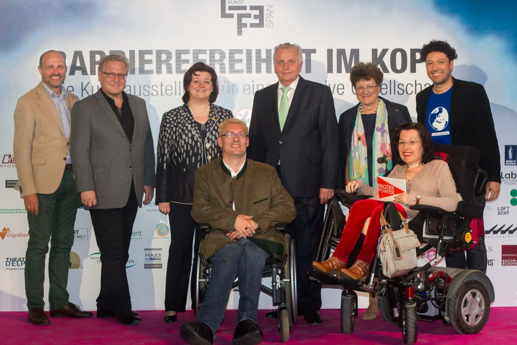 Barrierefreiheit im Kopf 2015: Gruppenfoto bei der Eröffnung vor der Festivalwand, zwei Personen im Rollstuhl