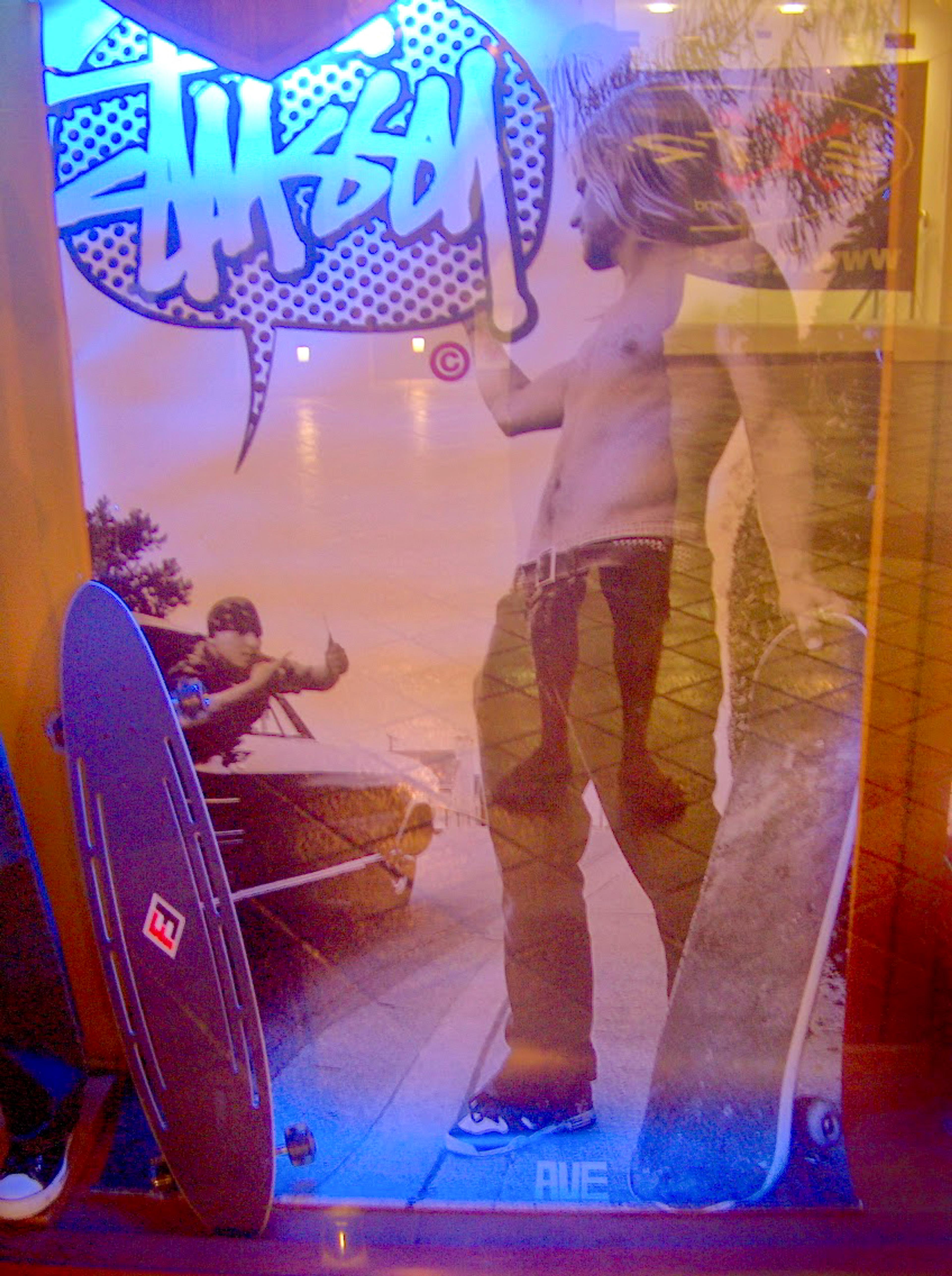 Ein Schaufenster mit einem großen Poster eines Skateboarders, der ein Skateboard hält, und einem weiteren Skateboard, das an der Seite lehnt.