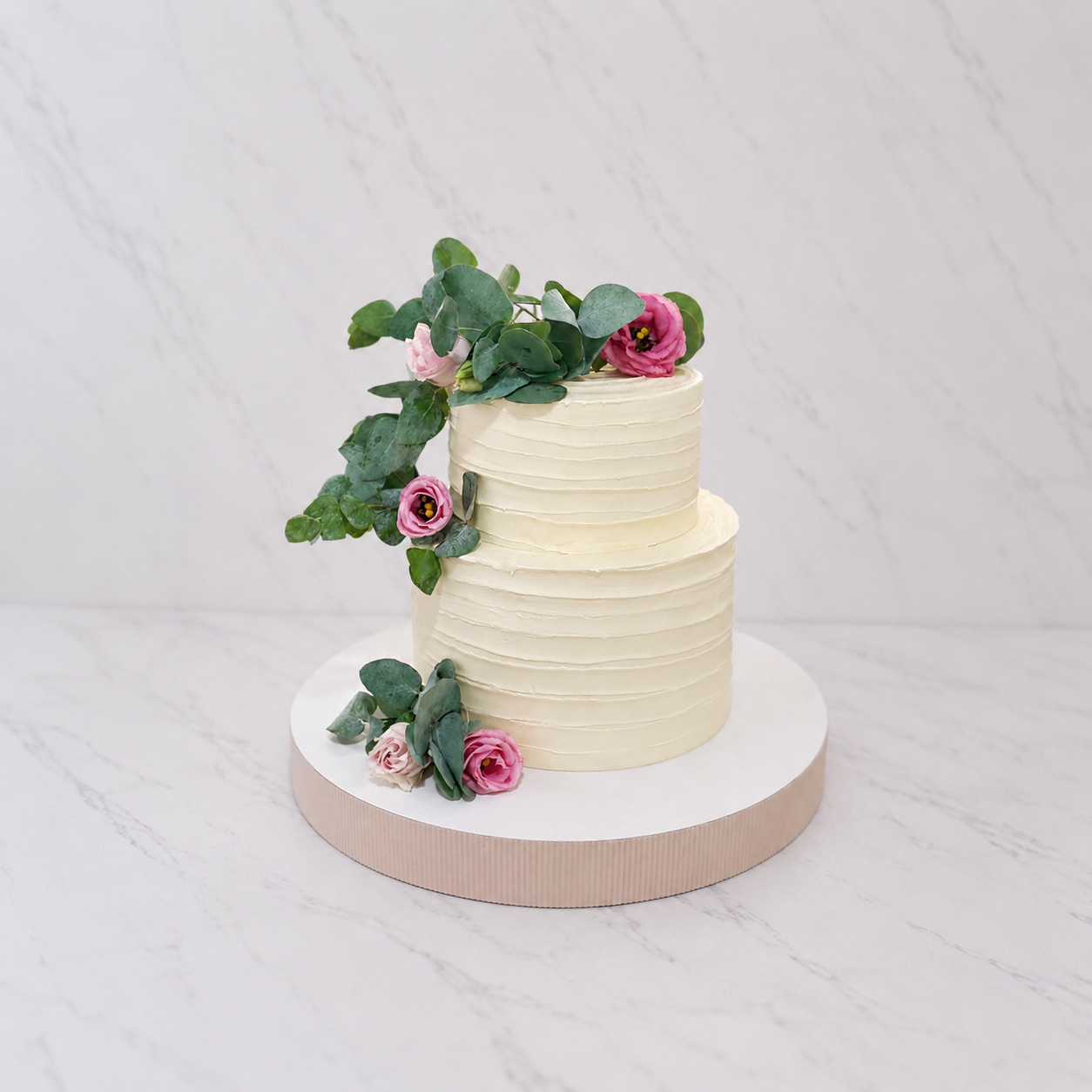 Tweelaagse bruidstaart met geribbelde ivoorkleurige botercrème, roze rozen en eucalyptus