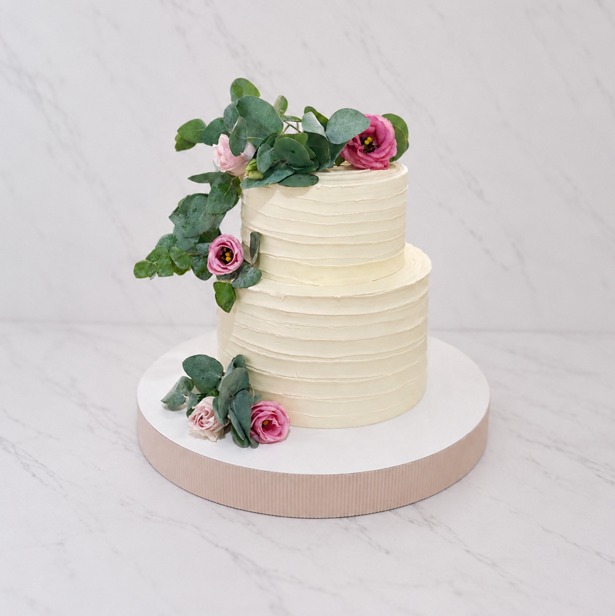 Tweelaagse bruidstaart met geribbelde ivoorkleurige botercrème, roze rozen en eucalyptus