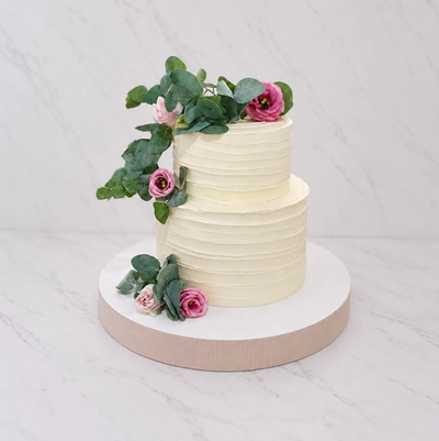 Tweelaagse bruidstaart met geribbelde ivoorkleurige botercrème, roze rozen en eucalyptus