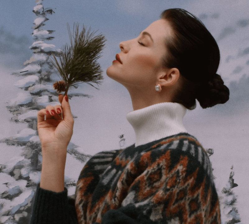 a woman in a sweater holds pine needles in her hand