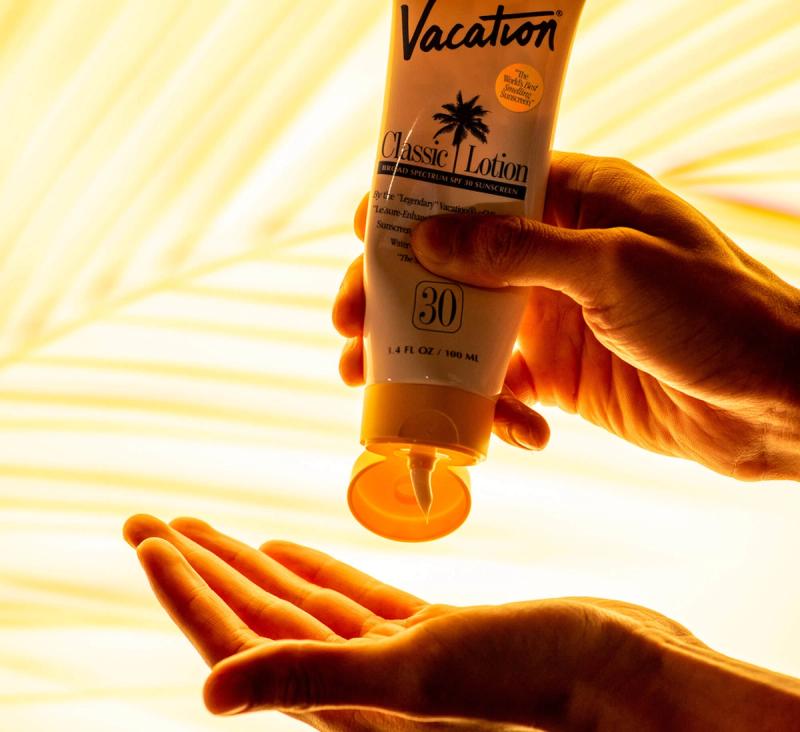 A hand squeezes Vacation brand sunscreen from a tube into an open palm.