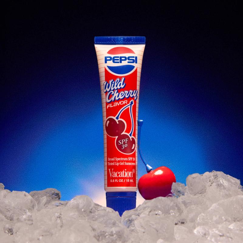 Pepsi Wild Cherry SPF 30 Tinted Lip Gel tube stands in ice with a red cherry against a blue background.