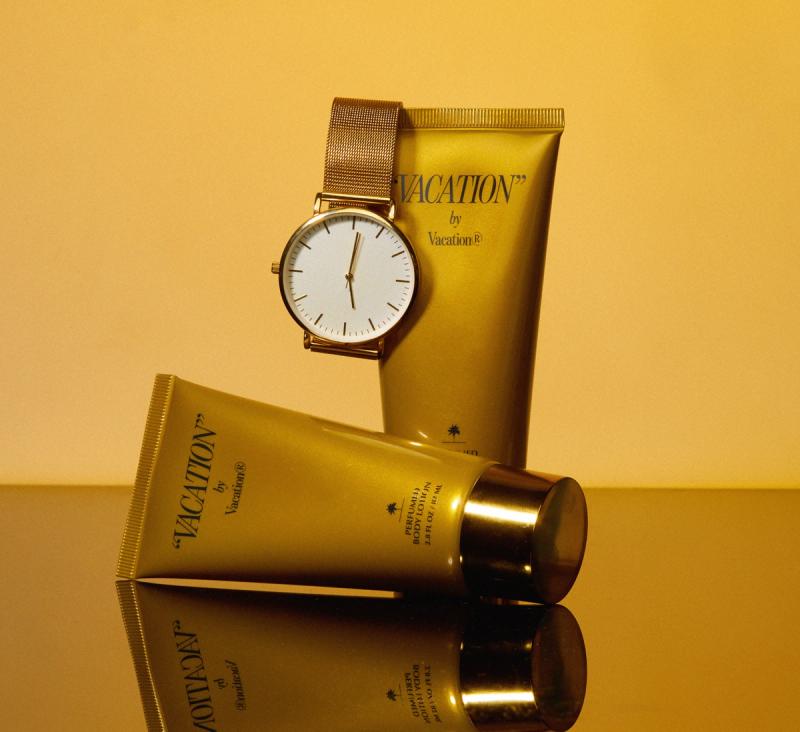 two gold tubes of "VACATION" by Vacation® Perfumed Body Lotion and a gold watch