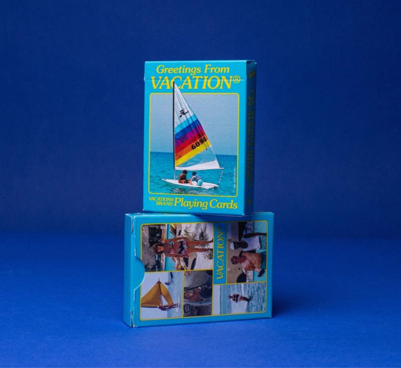 two boxes of greetings from vacation playing cards are stacked on top of each other on a blue surface .