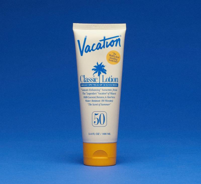 A white tube of Vacation Classic Lotion SPF 50 sunscreen with a yellow cap on a blue background.
