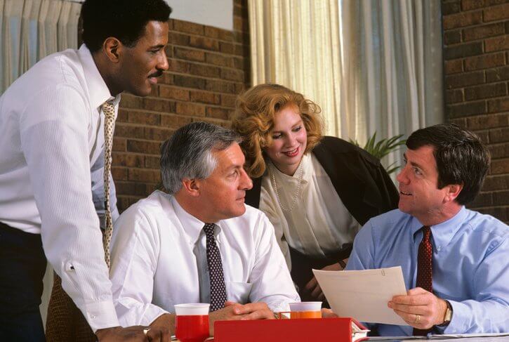 a group of business people are sitting around a table having a meeting .