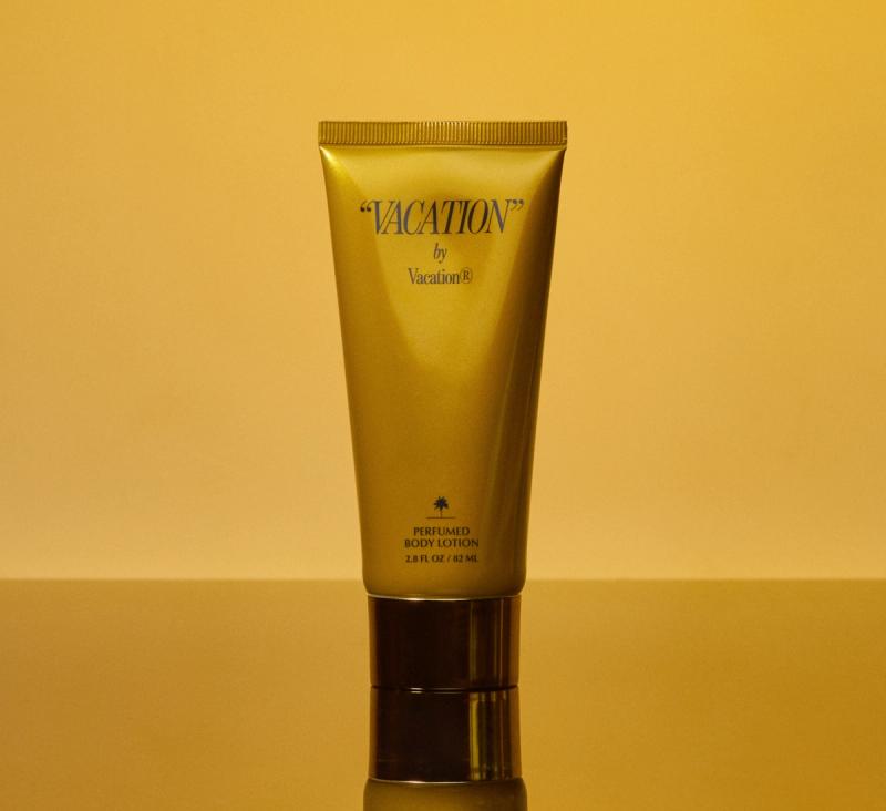 a gold tube of "VACATION" by Vacation® Perfumed Body Lotion on a mirrored gold surface