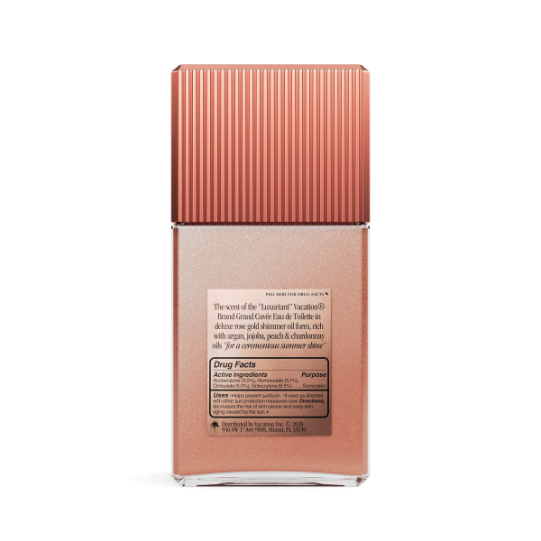 Back of a rectangular bottle of rose-gold shimmer oil with a ribbed cap, displaying a 'Drug Facts' label.