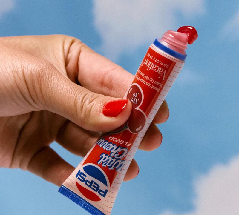 Hand holding a Pepsi® Wild Cherry lip gel against a blue sky with clouds