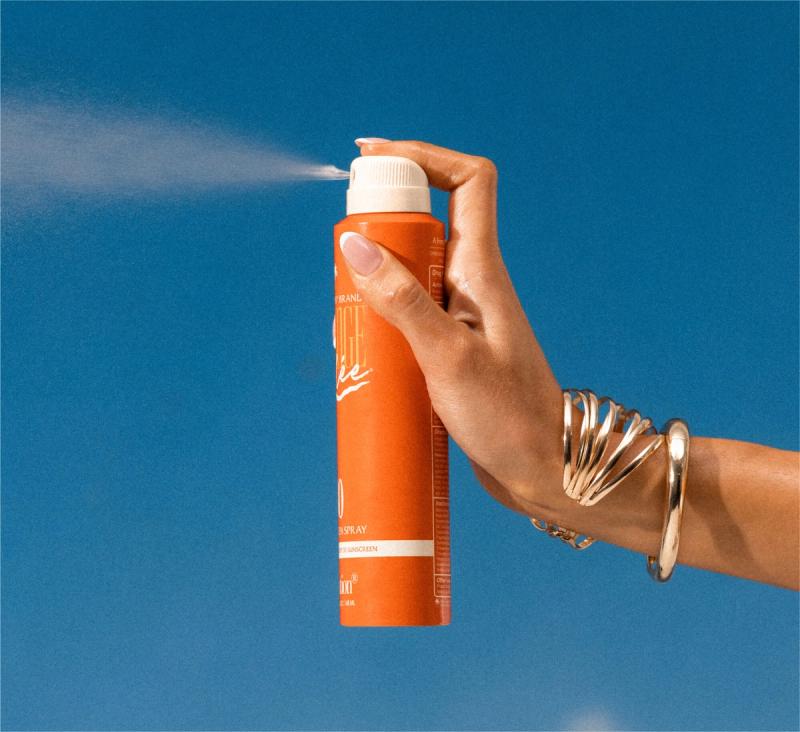 a woman is spraying Orange Gelée® SPF 30 Spray Oil with her hand