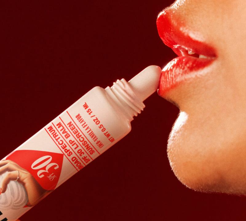 A close-up of a person applying SPF 30 vanilla lip balm to their glossy red lips.