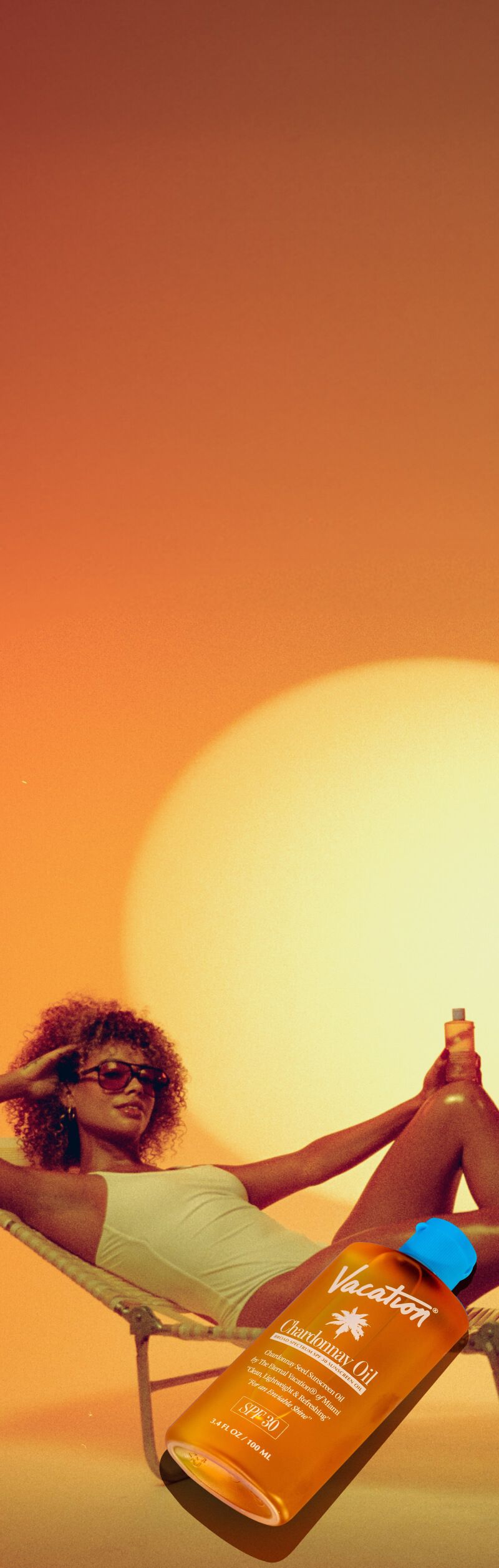 A woman in a white swimsuit lounges on a chair in the sunset