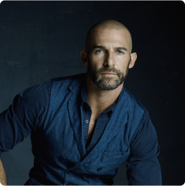 a bald man with a beard is wearing a blue shirt and vest