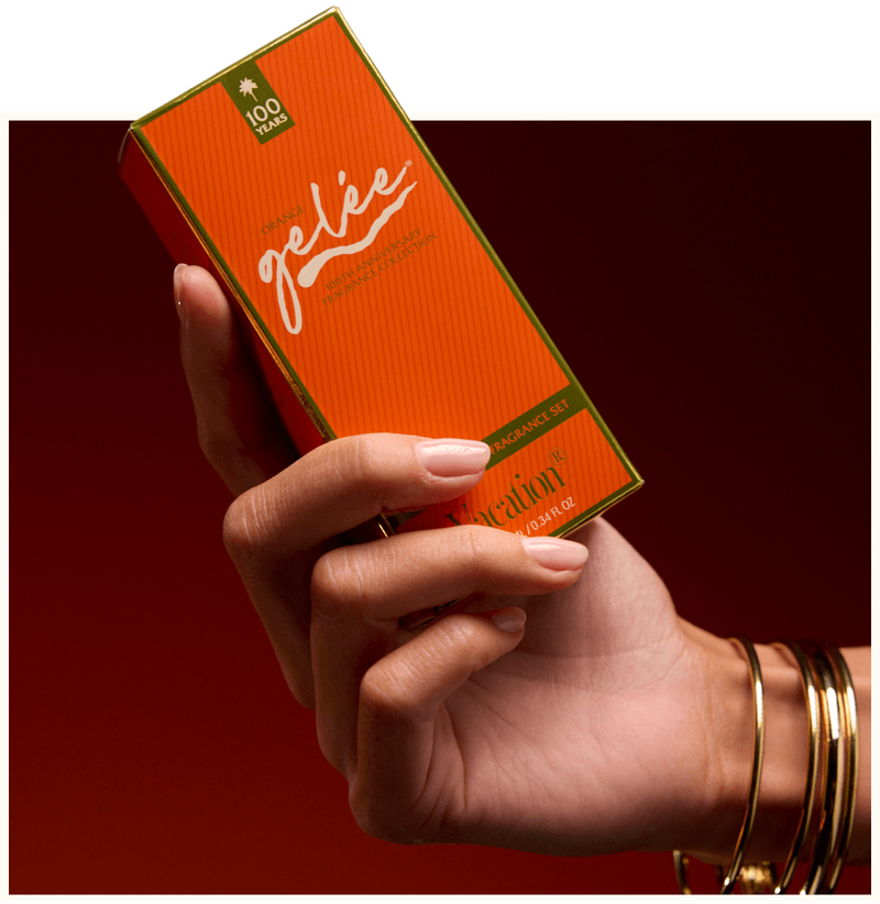 Hand holding an orange "Vacation Orange Gelée Fragrance Set" box, wearing gold bangles.