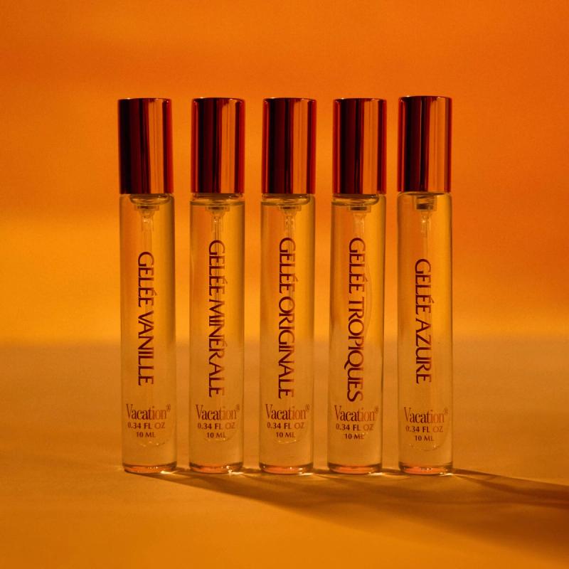 Five tall, slender perfume bottles with gold caps, labeled with different "Gelée" scents, stand in a line against a warm orange background.