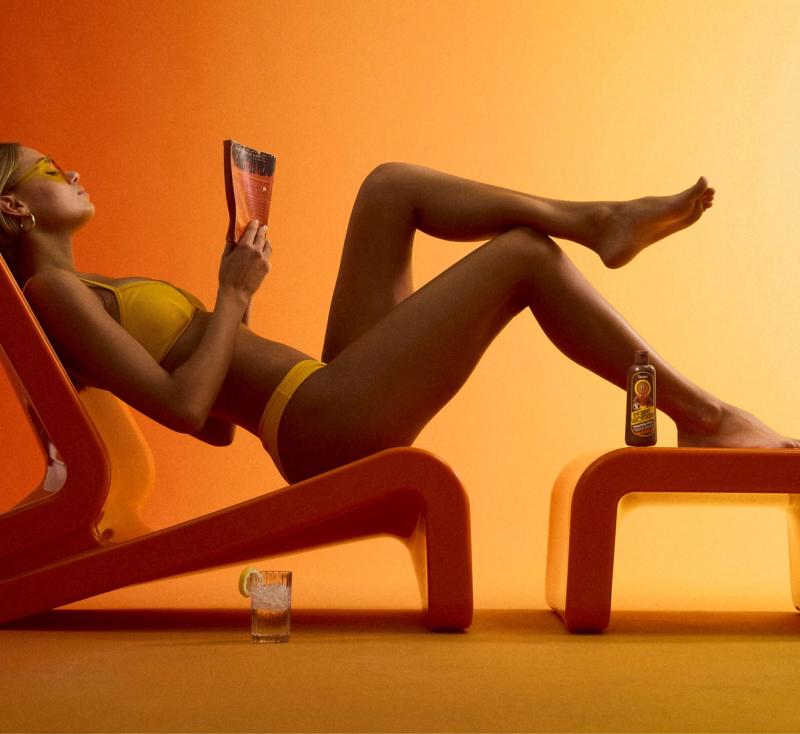 a woman in a bikini is laying in an orange chair reading a book .