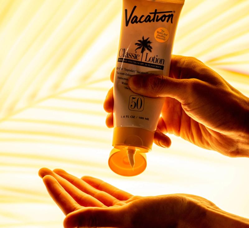 A hand squeezes Vacation Classic Lotion SPF 50 sunscreen into another open palm.
