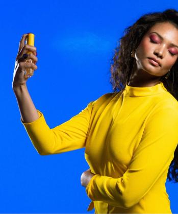 a woman in a yellow dress is spraying perfume on her face