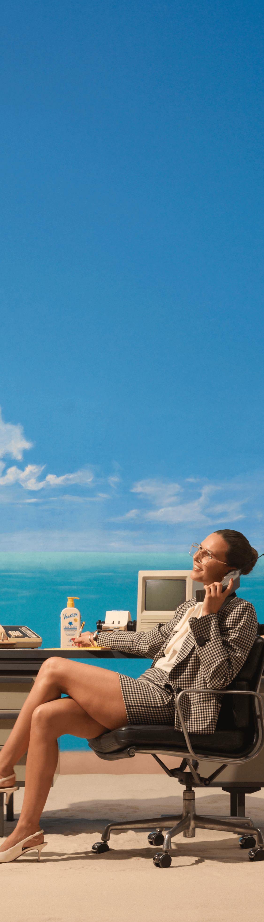 a woman sits at a desk on the beach talking on a cell phone