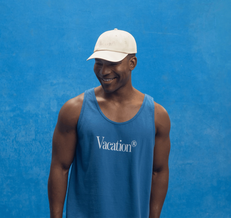 a man wearing a blue tank top and a Vacation® tone-on-tone hat