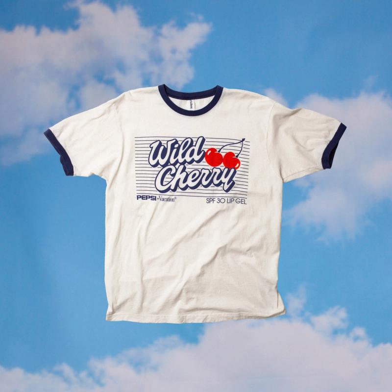 White ringer tee with blue trim featuring a "Wild Cherry" graphic with red cherries and Pepsi branding, floating against a blue sky with clouds.