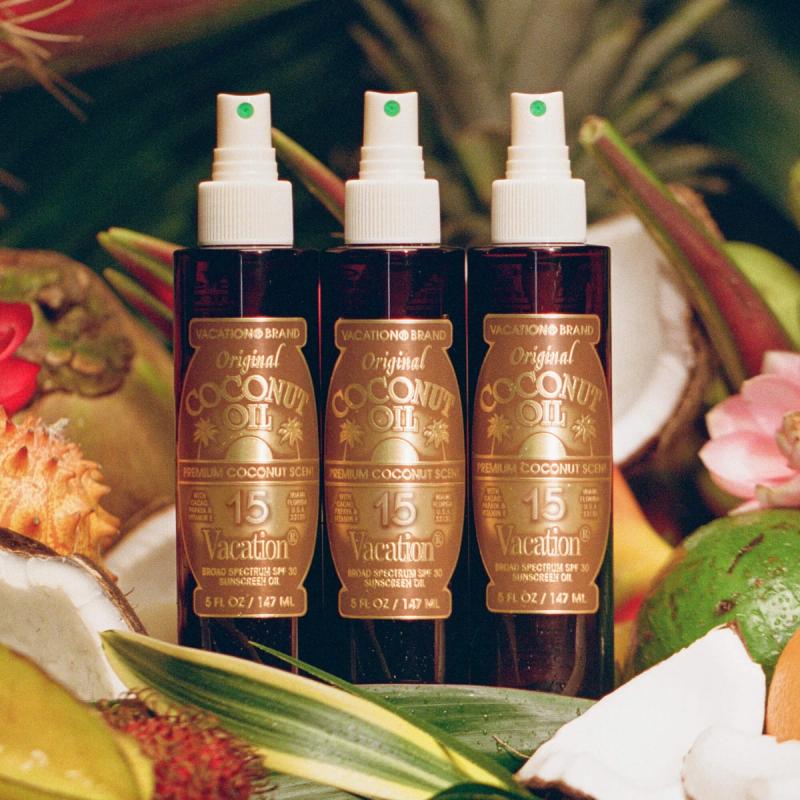 Three bottles of Vacation Brand Original Coconut Oil SPF 30 sunscreen amidst tropical fruits and foliage.