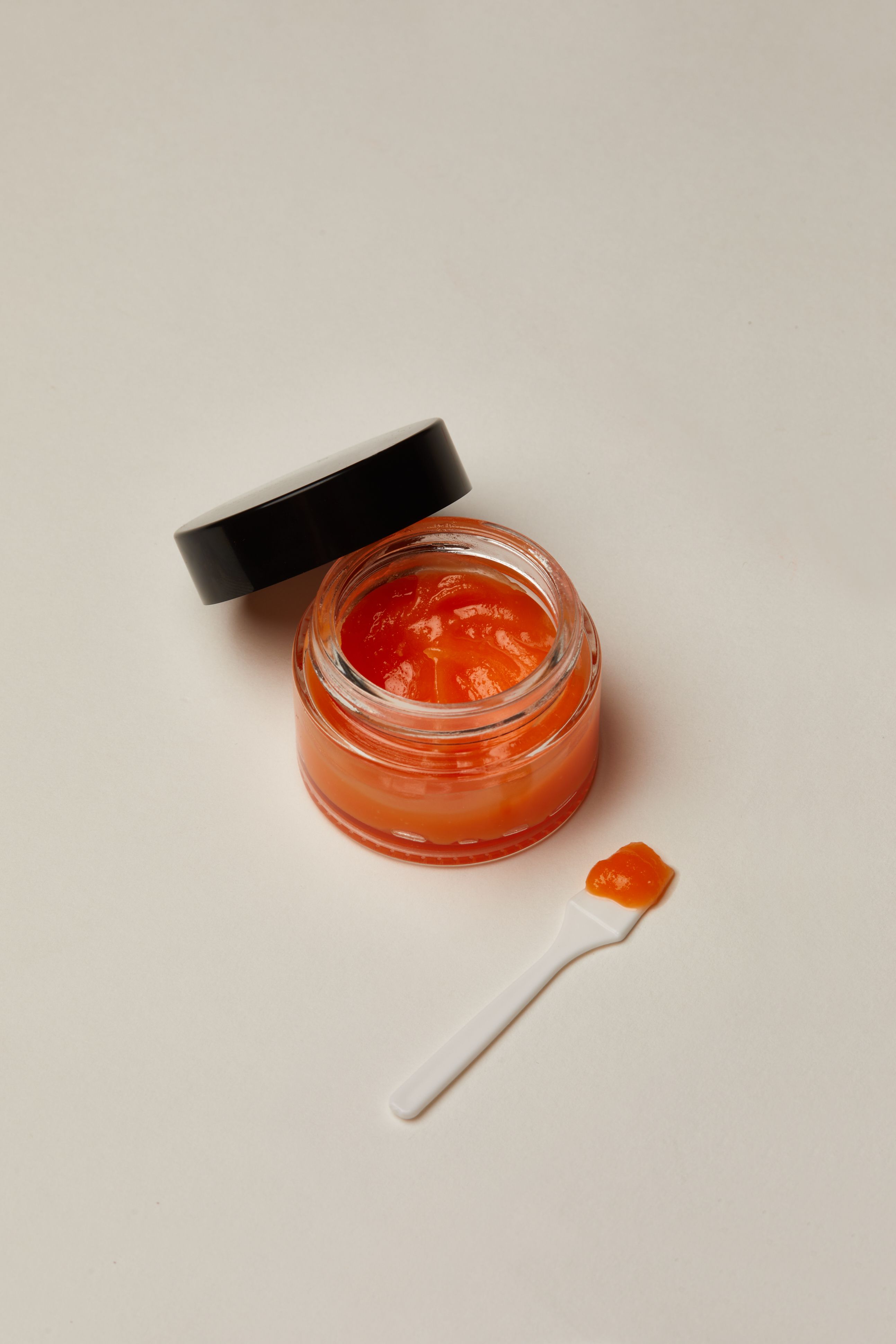 a jar of orange jelly next to a white spoon