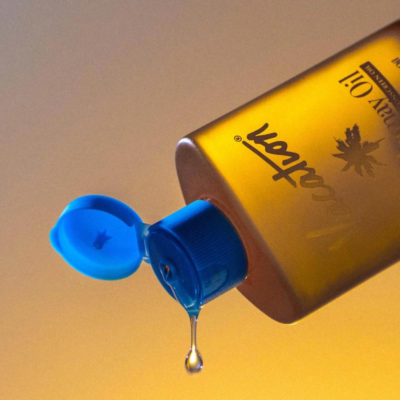 A golden bottle of Vacation Sunscreen Oil with an open blue cap, dripping a drop of oil.