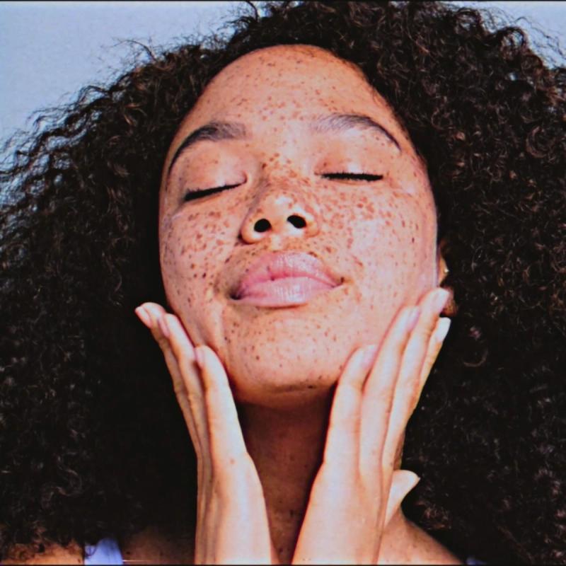 a woman with curly hair and freckles is touching her face with her hands .