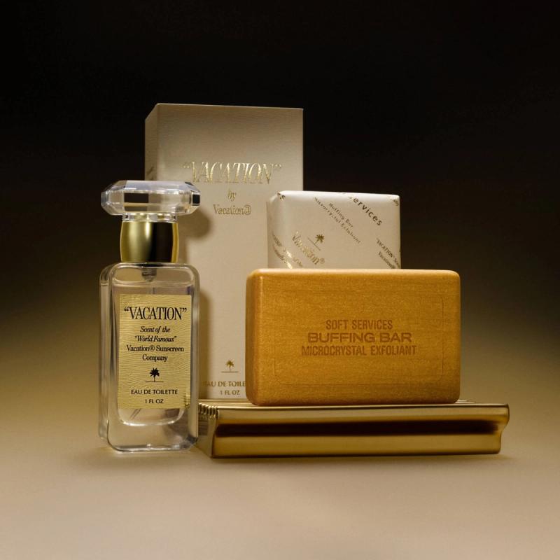 A golden-toned set of a "Vacation" perfume, "Soft Services" buffing bar, and wrapped soap on a tray.