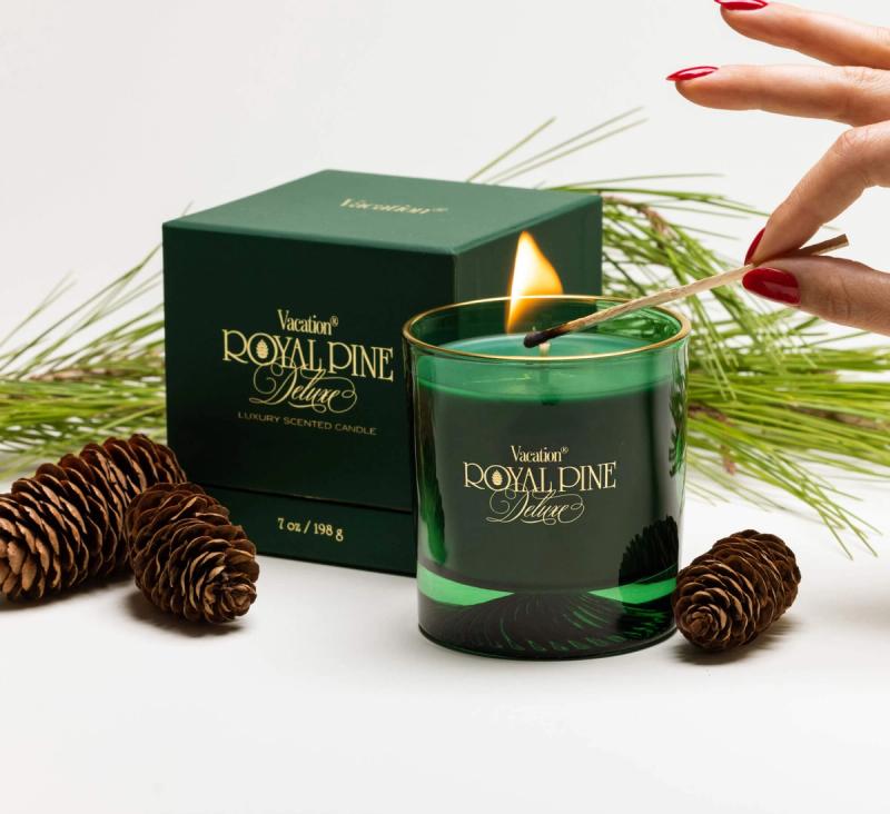 Royal Pine Deluxe candle and gift box with a hand and match, pinecones, and pine needles on a white background