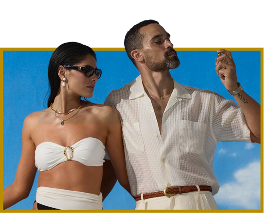 A woman in a white strapless top and sunglasses next to a man in a white shirt spraying fragrance, on a blue background.