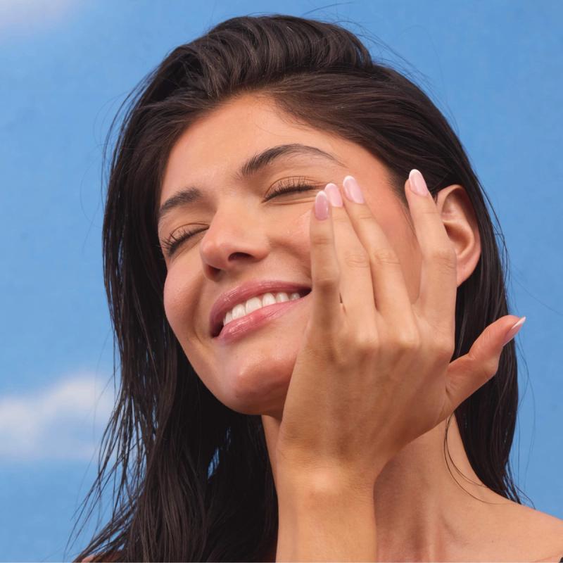 a woman is smiling while applying Vacation® Crystal SPF 50 Invisible Face Gel