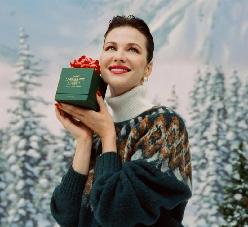 a woman in a green sweater is holding a green Royal Pine box with a red bow