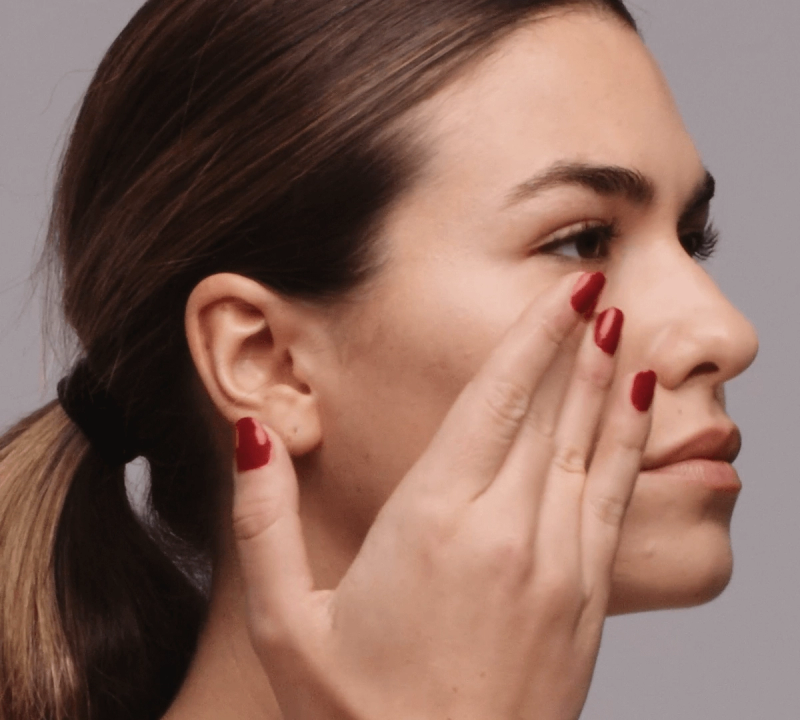 a woman with red nail polish touches her face